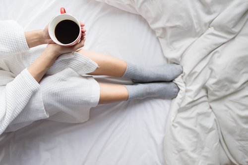 Woman getting cosy in bed with coffee and socks